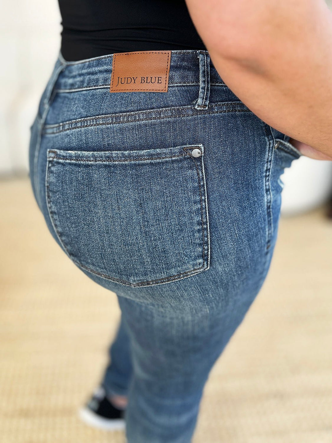 Dark slim jeans back pocket close-up with tan waistband label and button closure