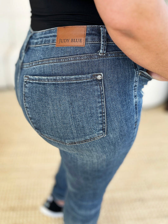 Dark slim jeans back pocket close-up with tan waistband label and button closure