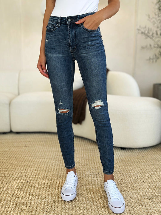 Dark wash mid waist slim jeans with torn knee detail and frayed ankle openings