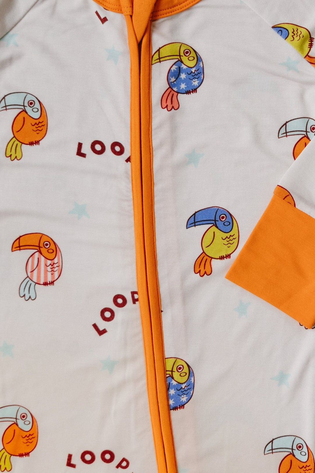 Close-up front: white romper with orange zipper trim and colorful bird print