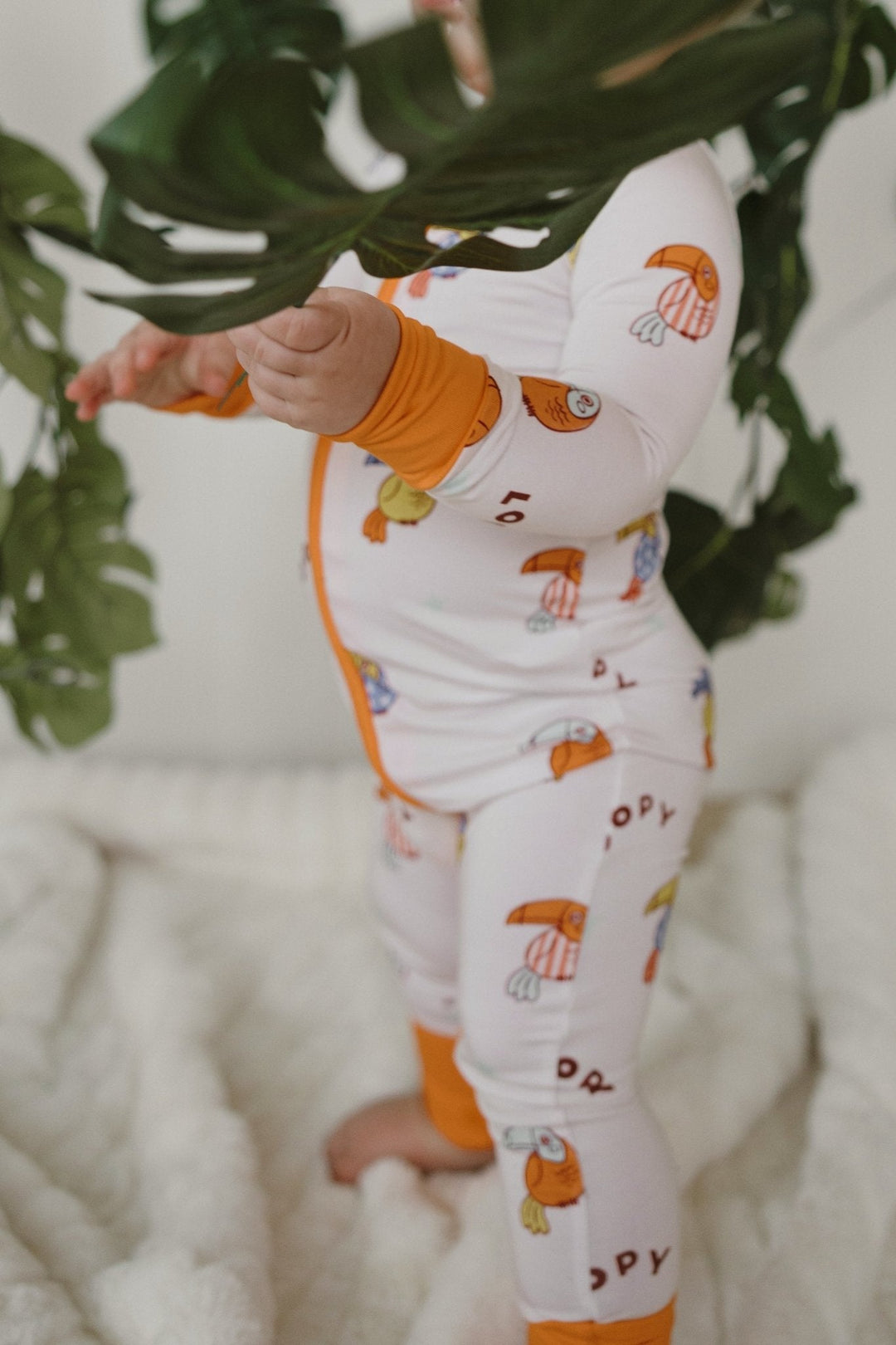 White zip-front romper with orange cuffs, long pants, colorful bird pattern
