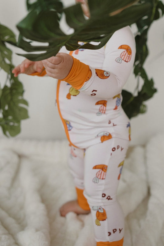 White zip-front romper with orange cuffs, long pants, colorful bird pattern