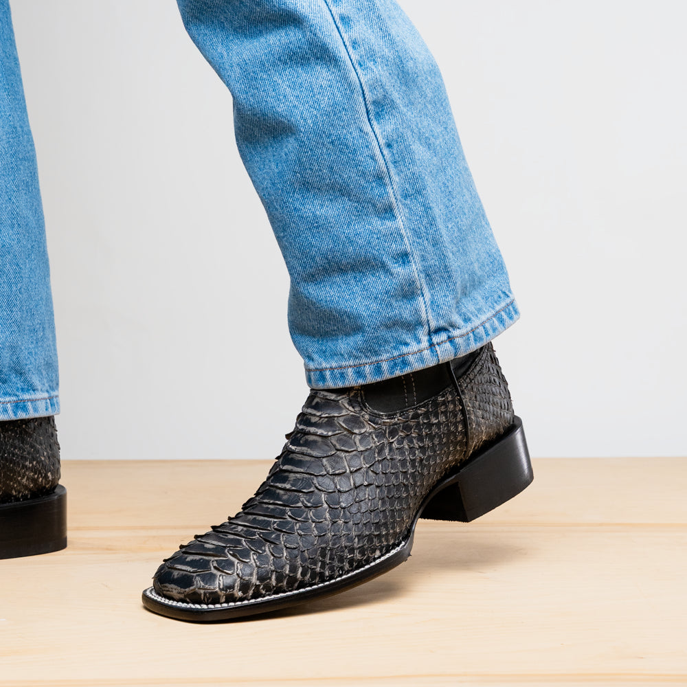 Close-up of black boot toe and heel; textured scale finish with white edge stitching