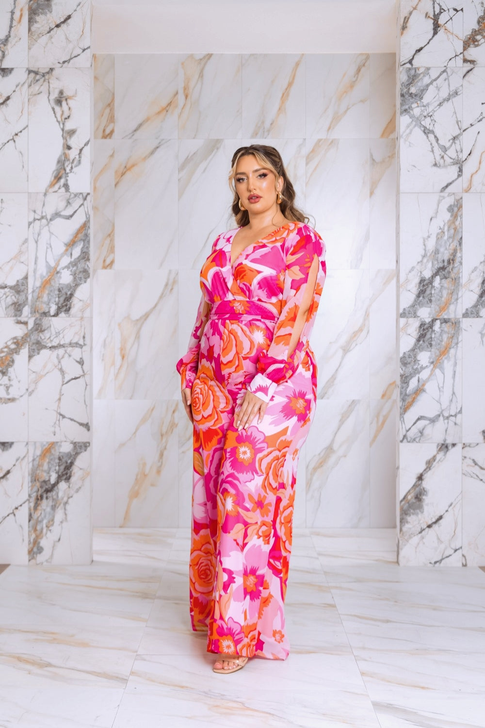 Pink floral plus-size jumpsuit with V-neck and long bishop sleeves, standing front
