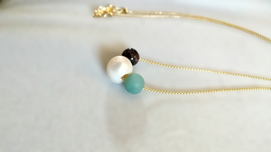 Gold chain necklace with white pearl, turquoise bead, and dark bead along the chain