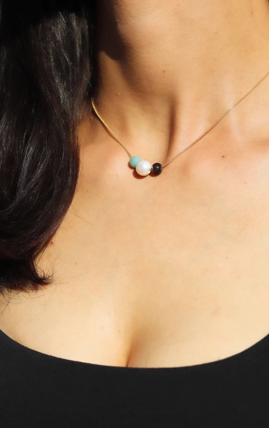 Gold chain necklace on skin with three beads: turquoise, white pearl, and dark bead