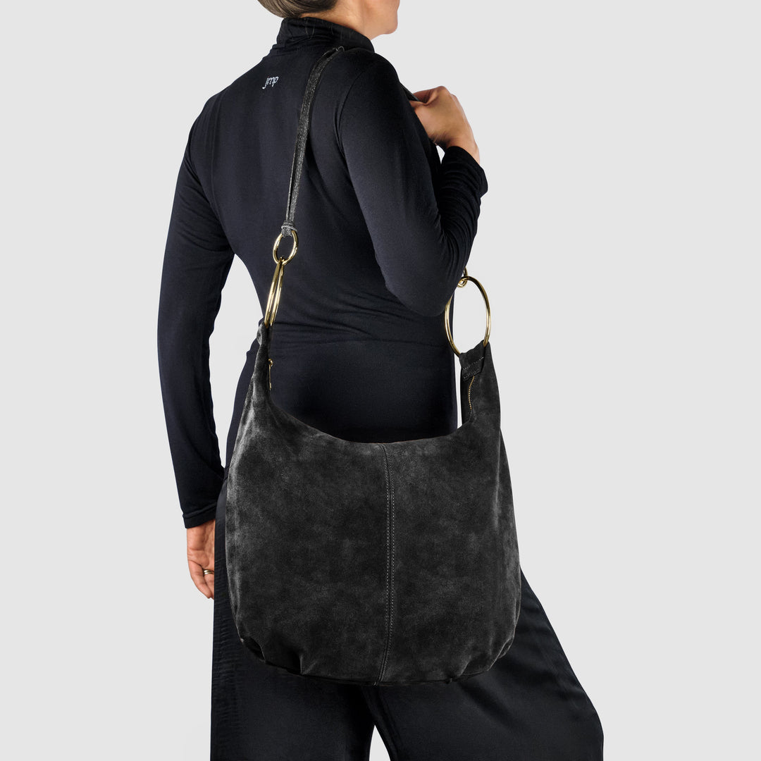 Black suede hobo bag worn crossbody-style with gold ring handles and open rounded body