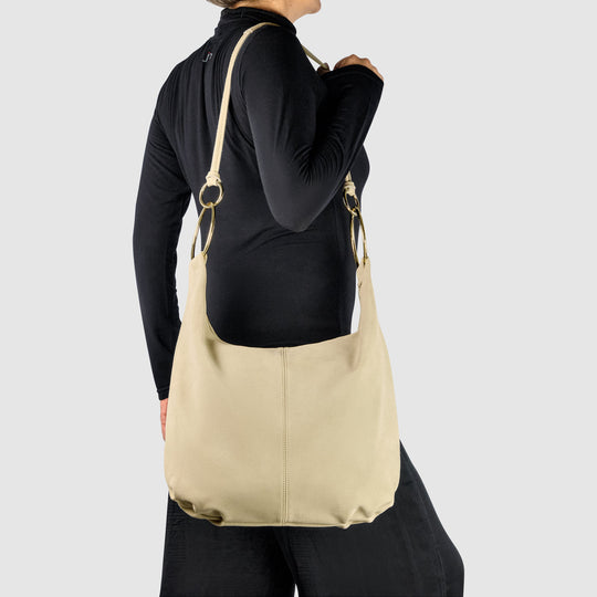 Beige suede hobo bag worn on shoulder with gold-tone ring straps