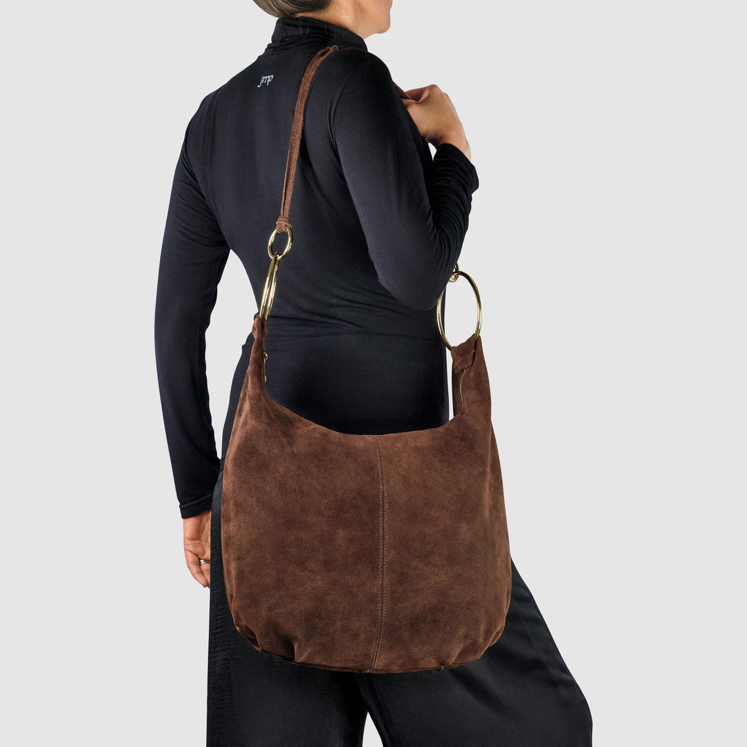 Brown suede hobo bag worn crossbody with gold-tone rings and round handle