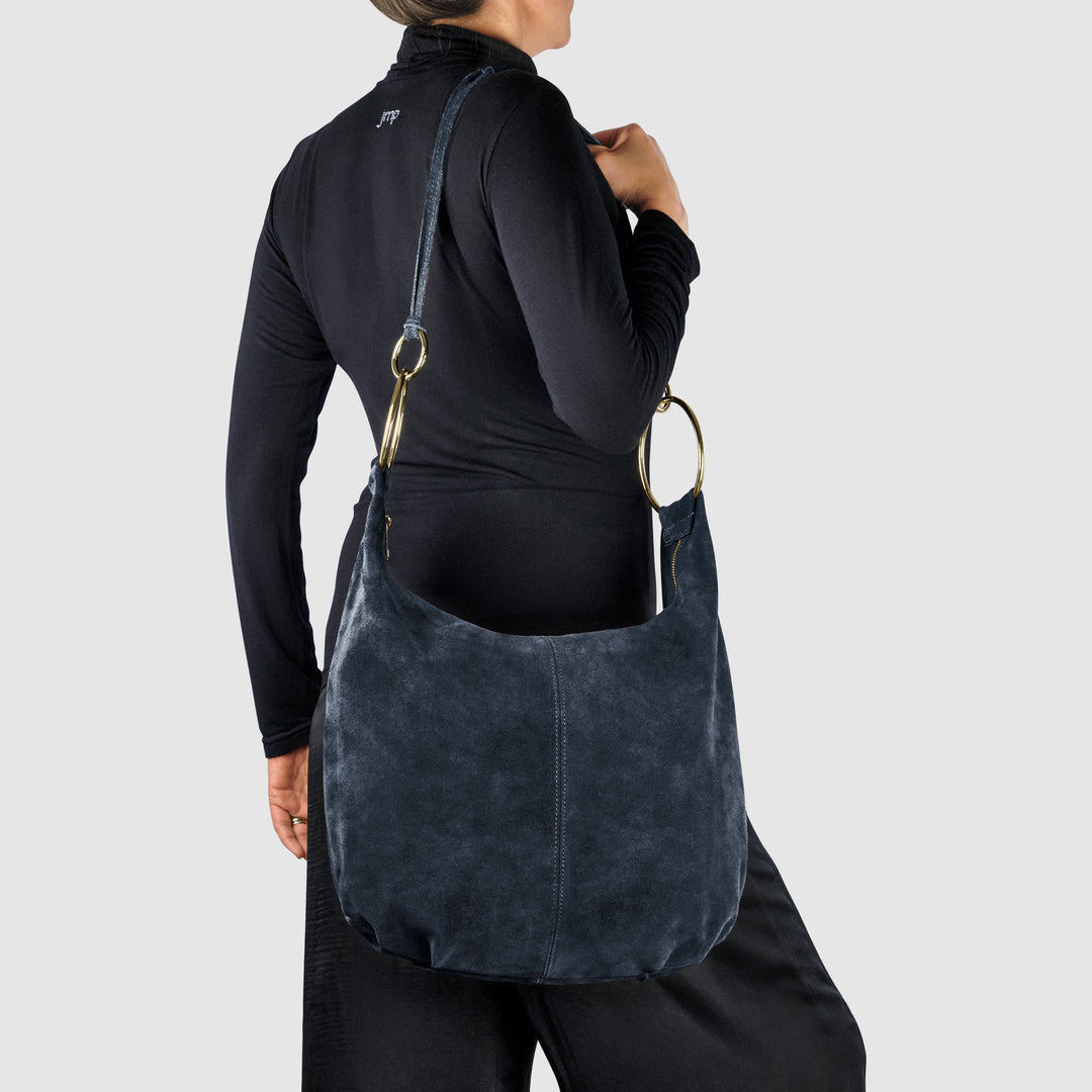 Dark blue suede hobo bag worn on shoulder with gold-tone ring straps