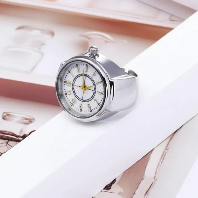 Silver quartz ring watch on white surface, crown and band details visible